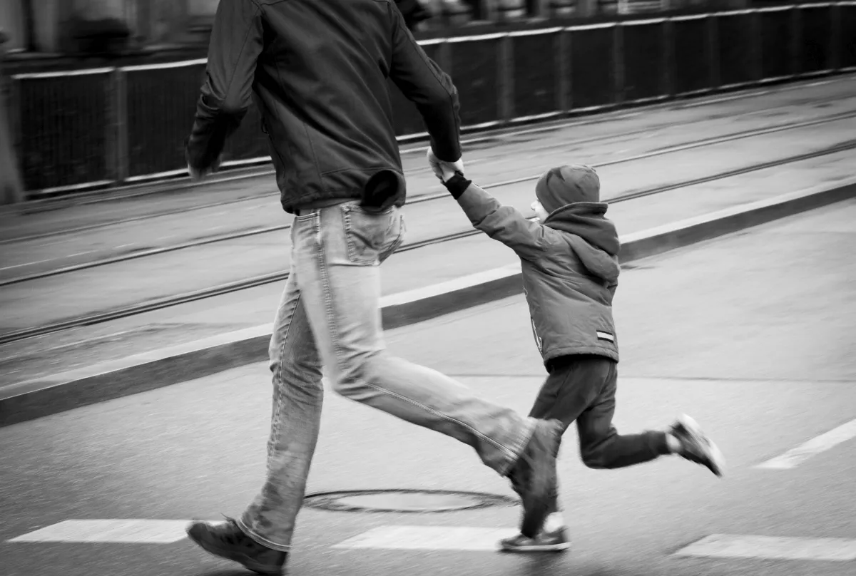 Adult pulling a running child by the hand across wet tram tracks